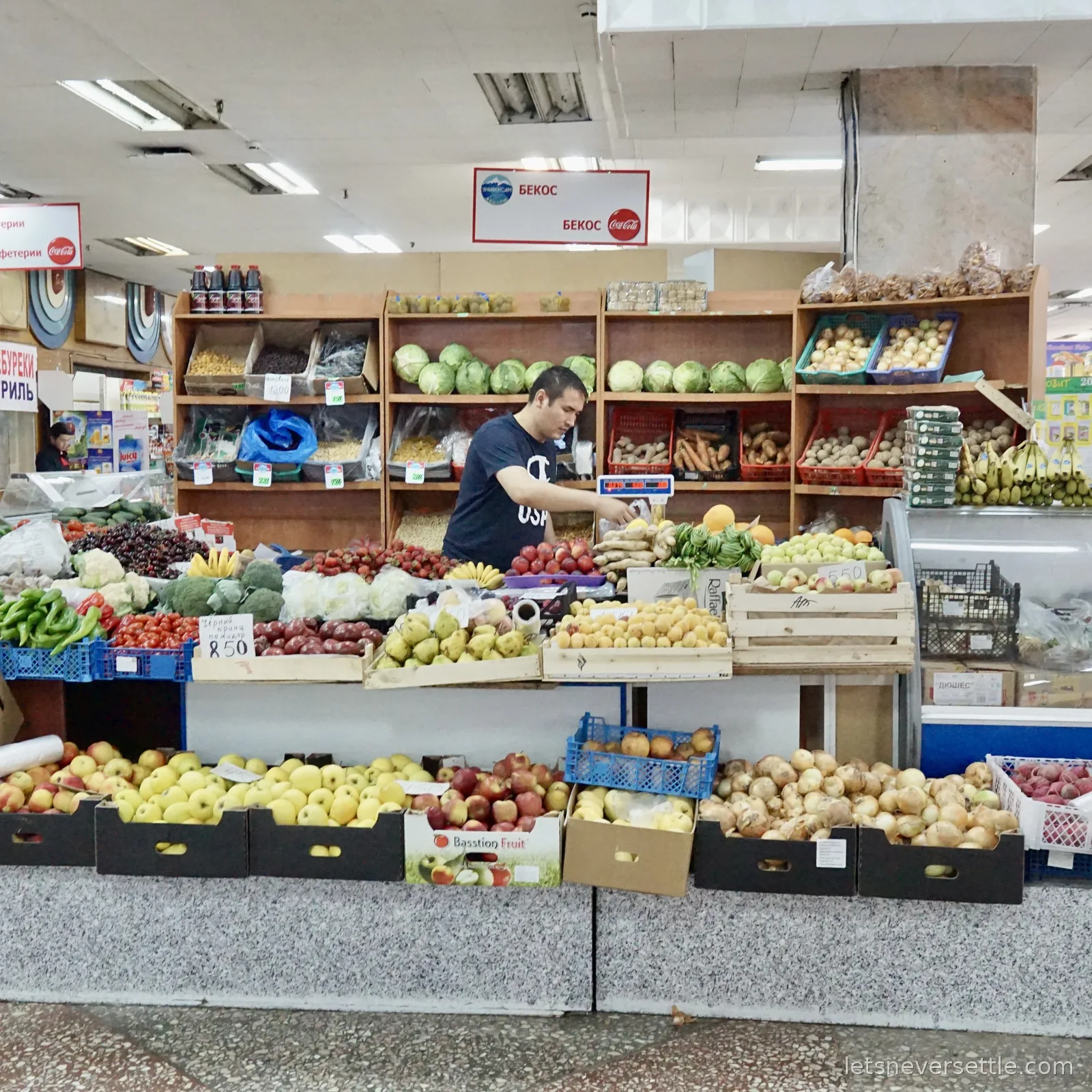 A produce stall stacked with cherries, strawberries, apricots, pears and cabbages, the seller reaching over the scales