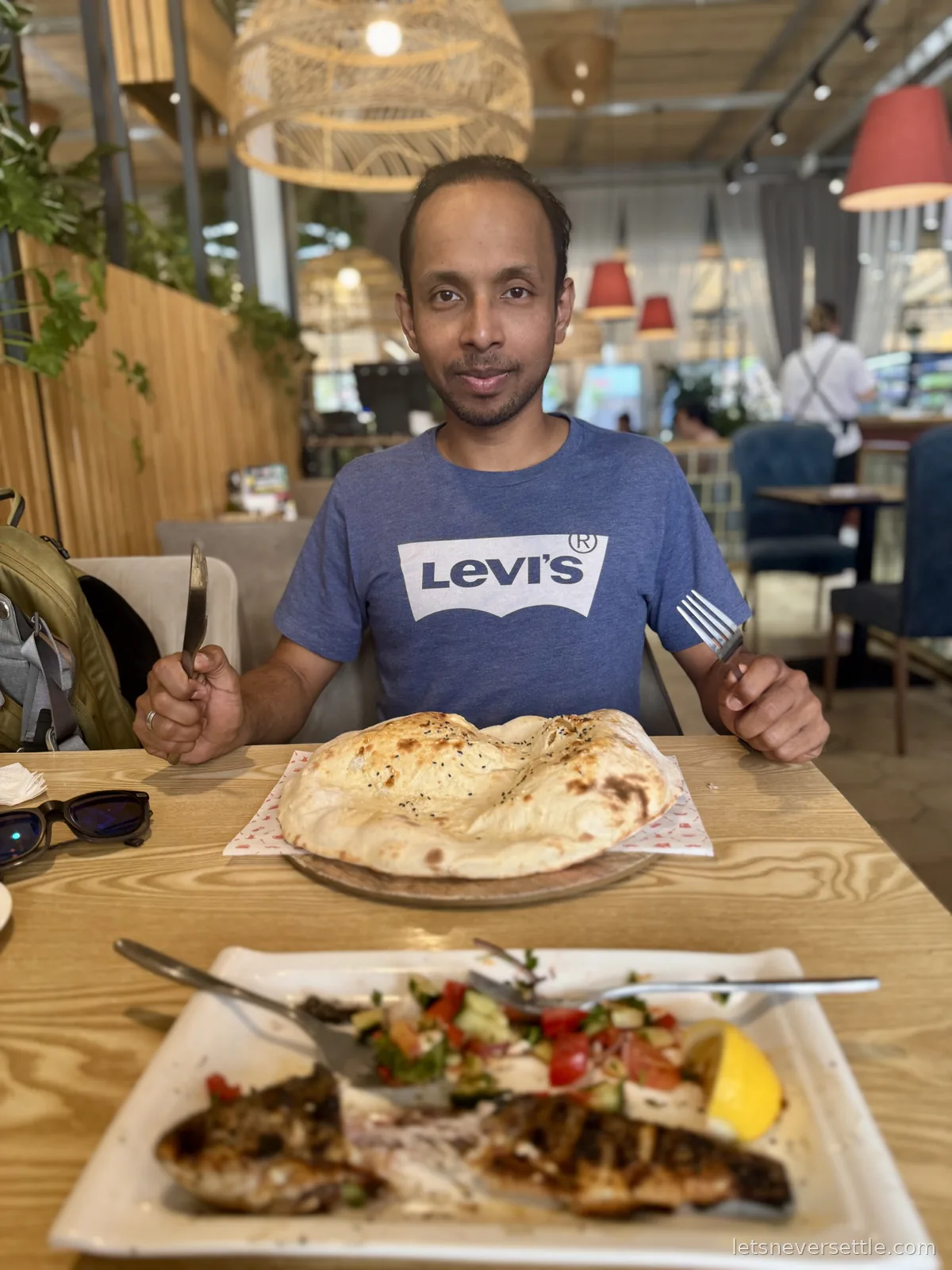 Dileep holding a knife and fork behind a huge puffed tandyr flatbread, with the finished fish platter in front of him