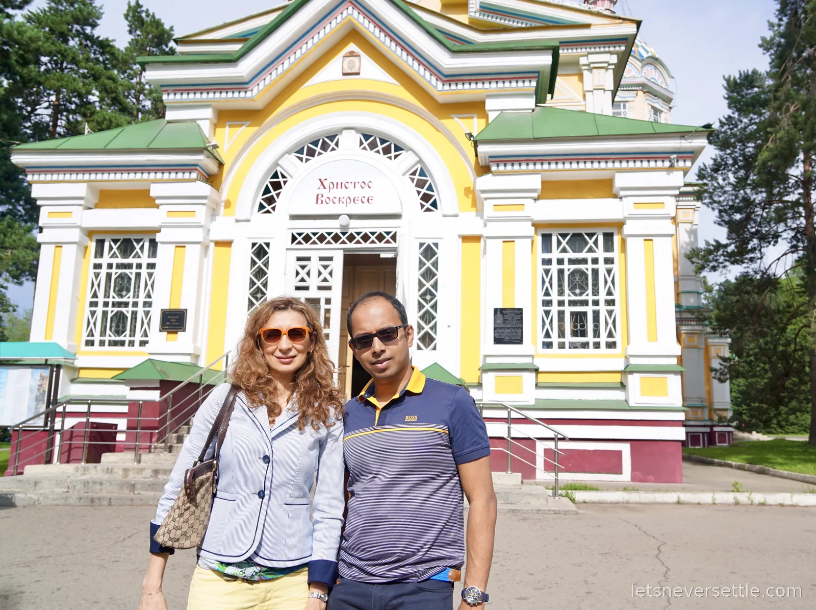Inga and Dileep standing in front of the cathedral entrance, a white arch with Cyrillic lettering above the open doorway