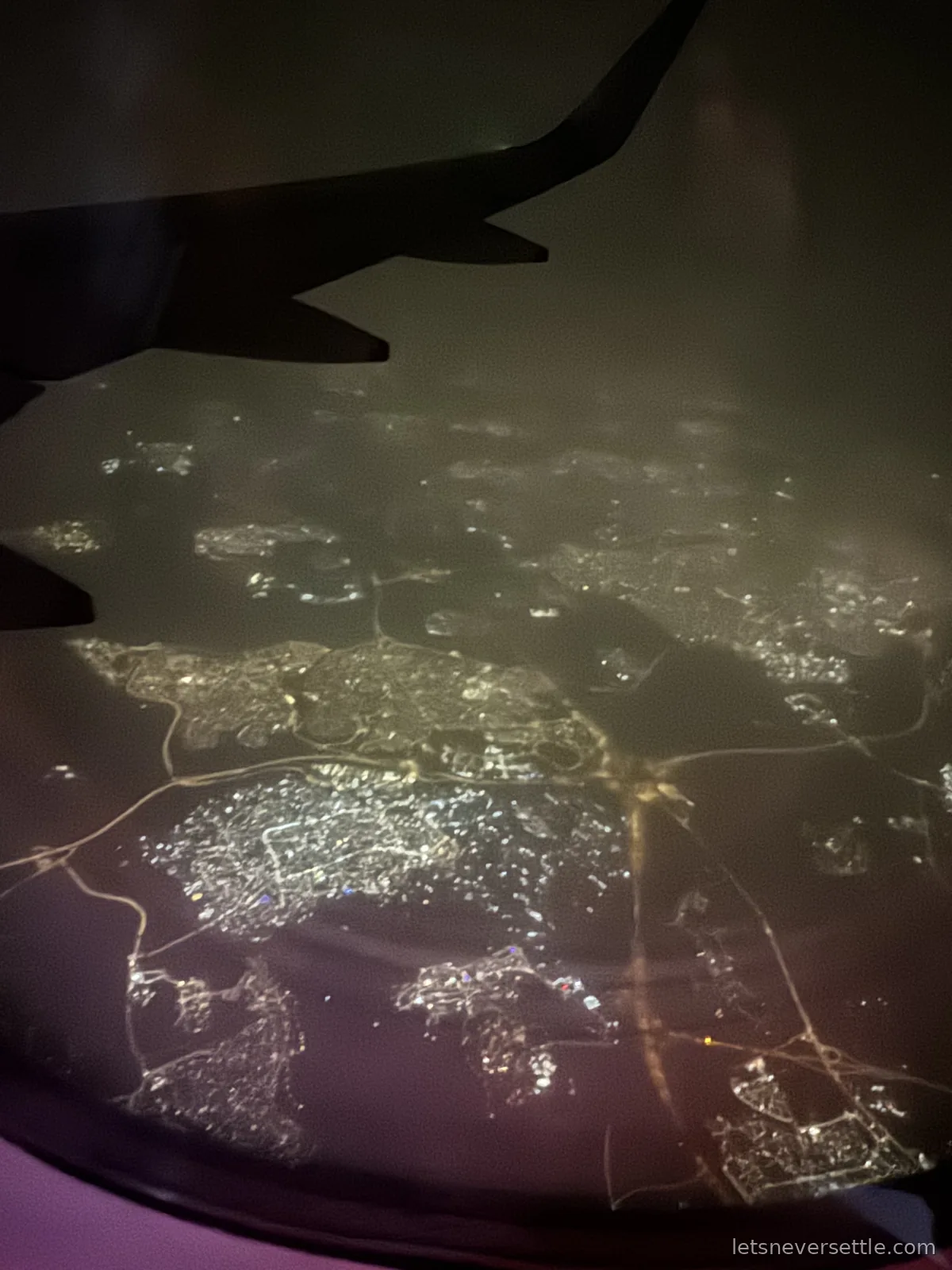 Night view from a plane window over Amman, the dark wing above a grid of orange and white city lights