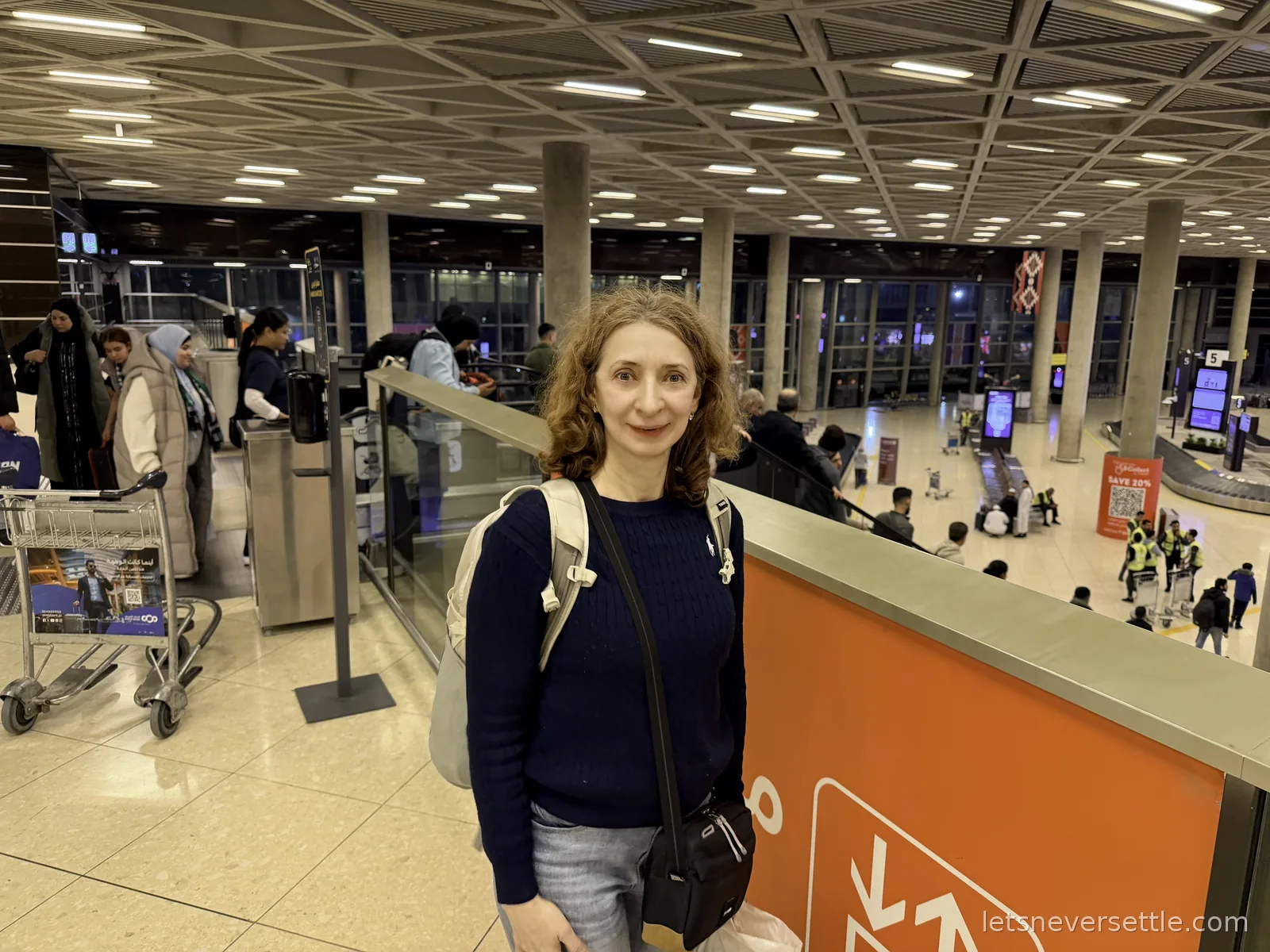 Inga standing on the walkway above the baggage hall at Queen Alia International Airport in Amman, carousels and passengers below her