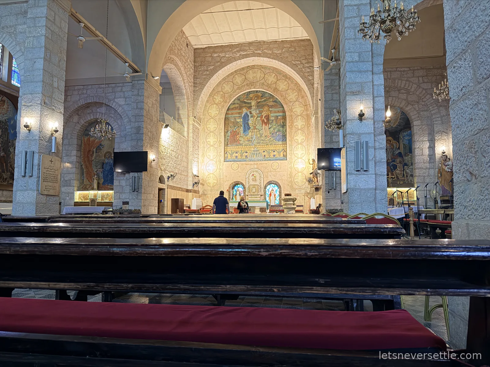 The interior of the Church of St John the Baptist in Madaba, with dark wooden pews and a large gold and blue mosaic arch above the altar
