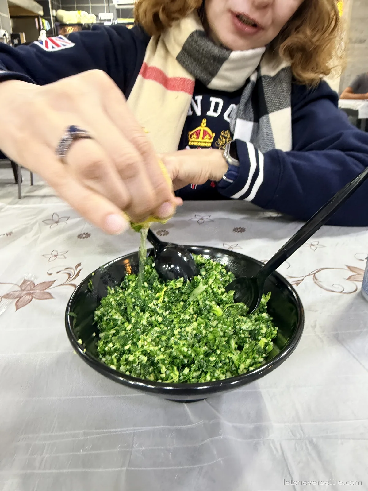 Inga squeezing a lemon over a black bowl of finely chopped tabbouleh on a restaurant table in Amman