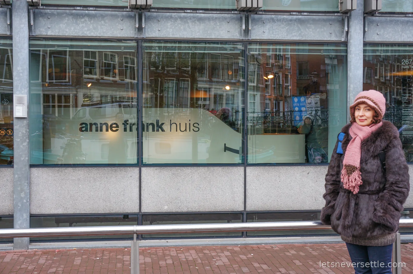 Inga in a pink hat and scarf standing outside the glass front of the Anne Frank Huis