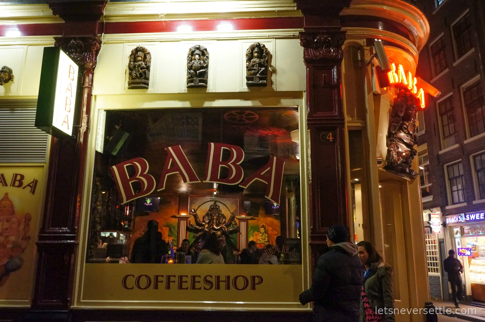 The neon-lit corner of Baba Coffeeshop at night, with carved wooden deity figures set into the cream facade