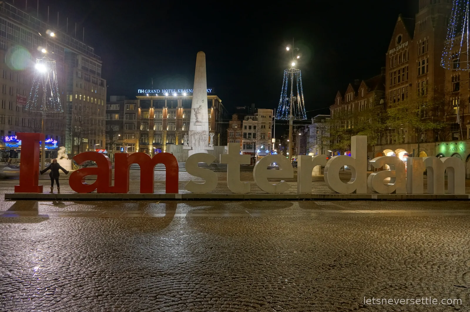 The giant I amsterdam letters on Dam Square at night with the National Monument and Christmas lights behind
