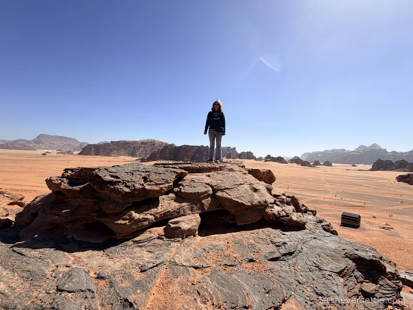 Inga standing on a dark rock outcrop in Wadi Rum, looking out over an open plain of red sand towards distant mountains