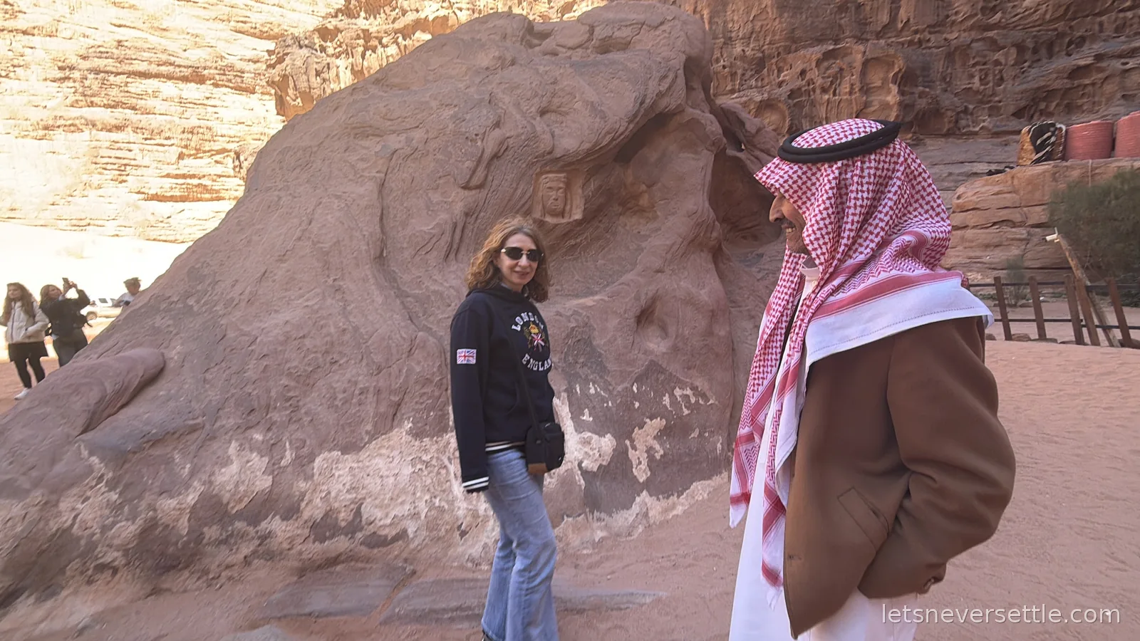 Inga standing beside a large boulder in Wadi Rum carved with ancient figures, her Bedouin guide in a red checked keffiyeh in the foreground