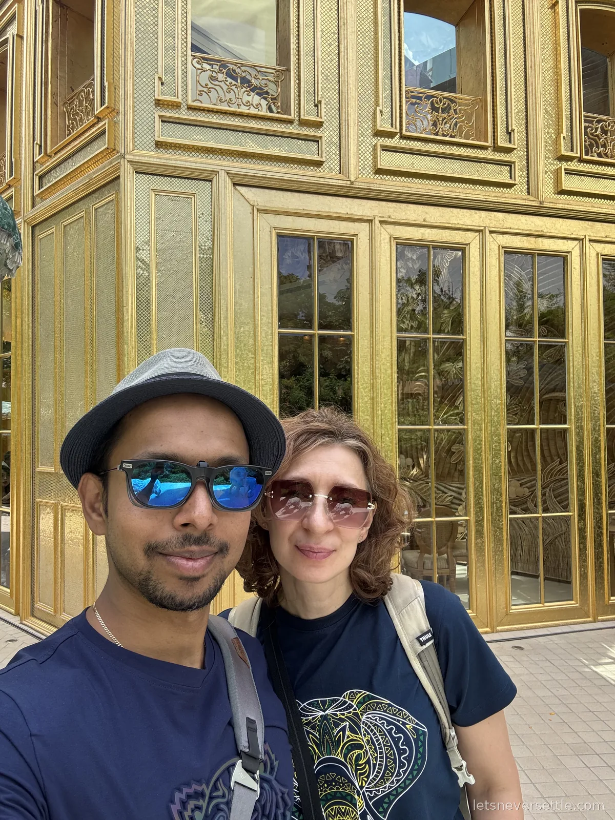 Selfie of Dileep and Inga in sunglasses in front of a tall gilded facade of gold panels and mirrored windows