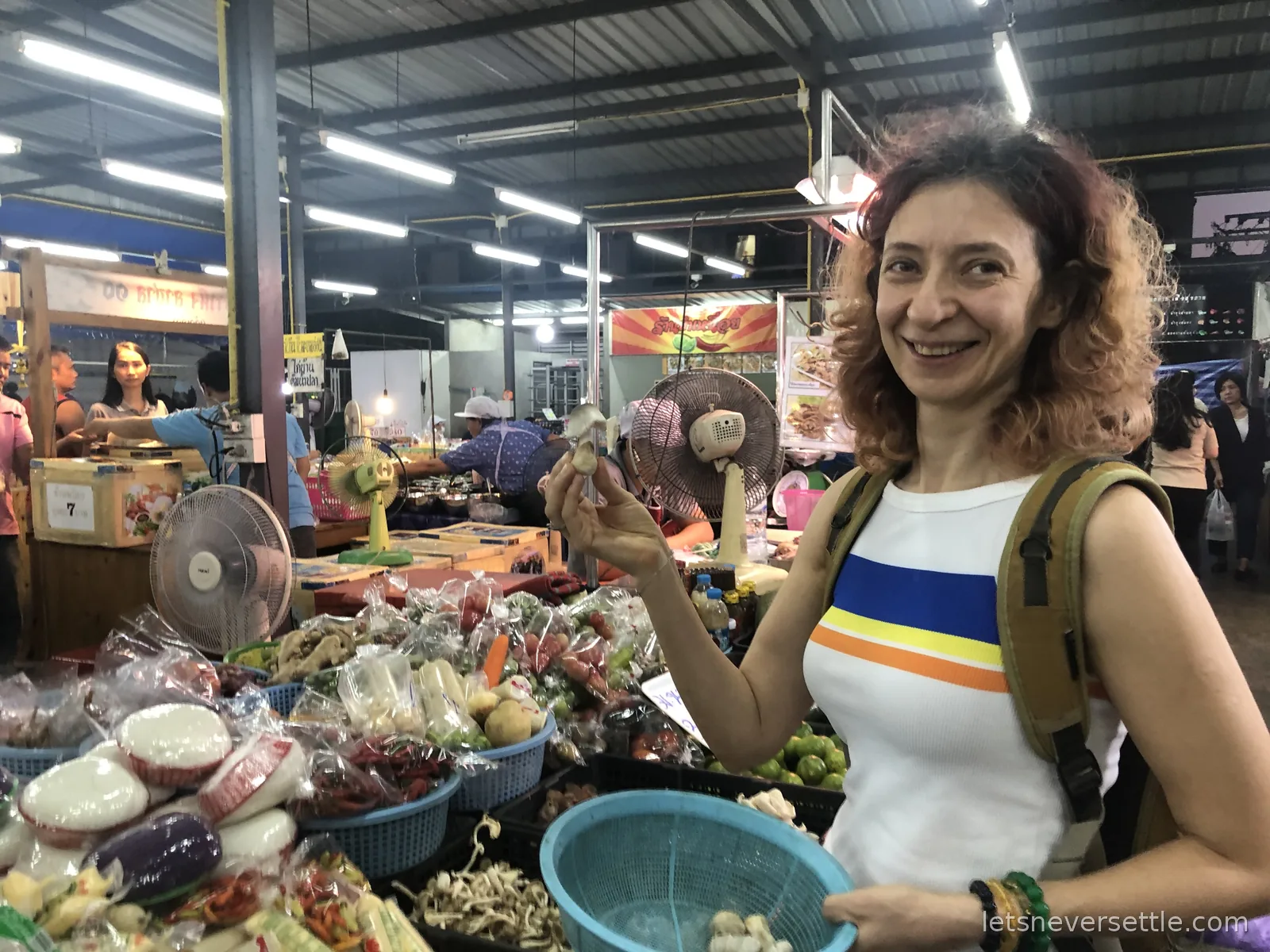 Inga holding up an oyster mushroom over baskets of chillies, limes and vegetables in a covered fresh market