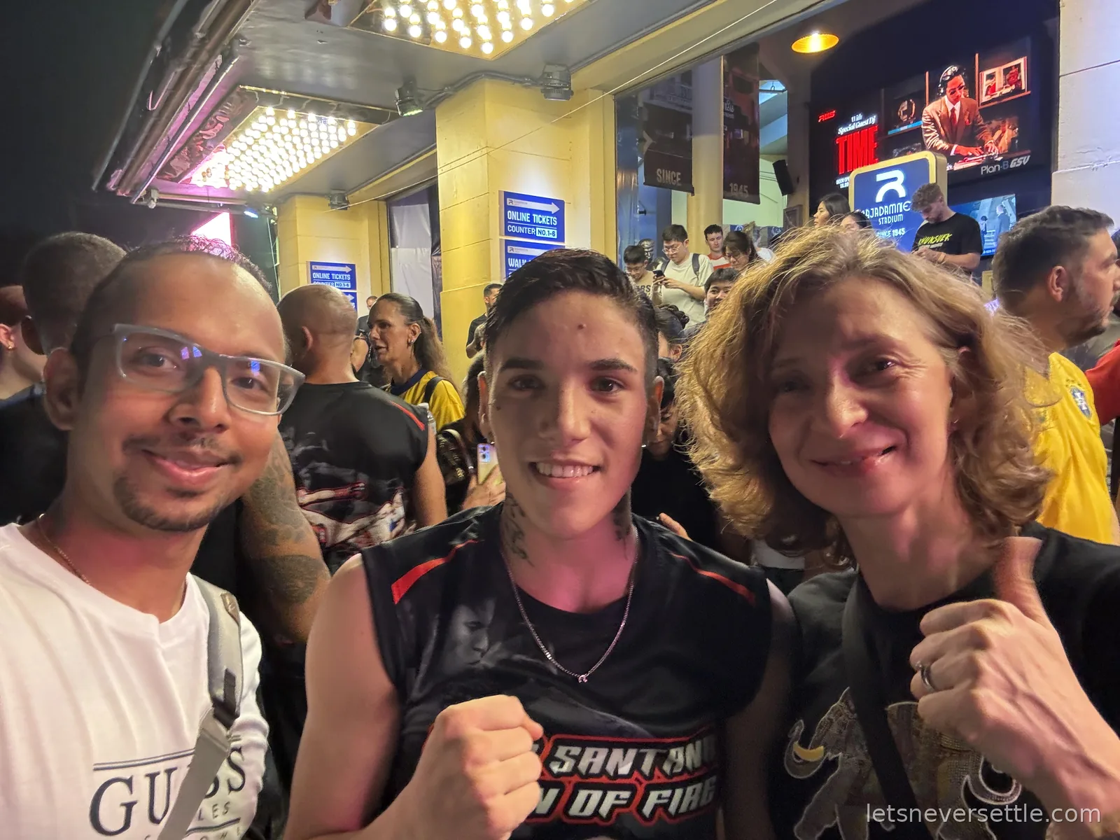 Dileep and Inga posing with a Muay Thai fighter under the marquee lights of the Rajadamnern Stadium ticket hall