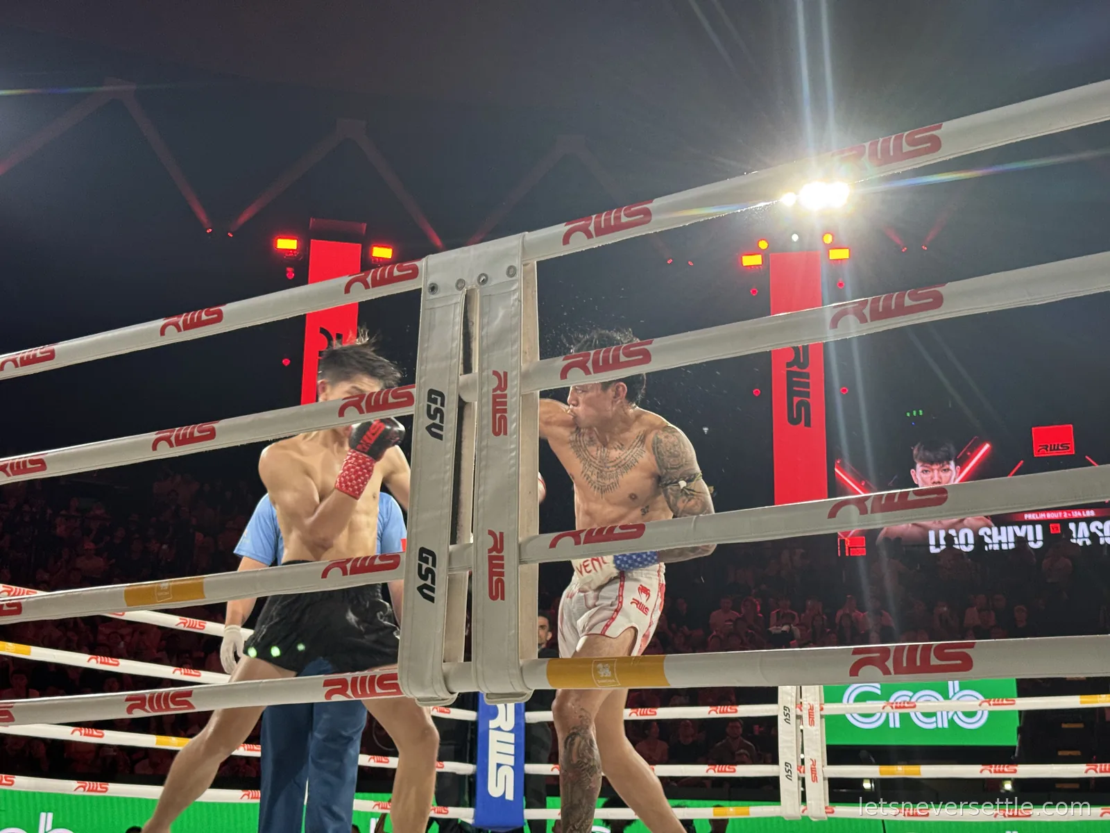 Two male Muay Thai fighters mid-exchange in the ring at Rajadamnern Stadium, one throwing a punch, sweat flying, the referee stepping in behind them