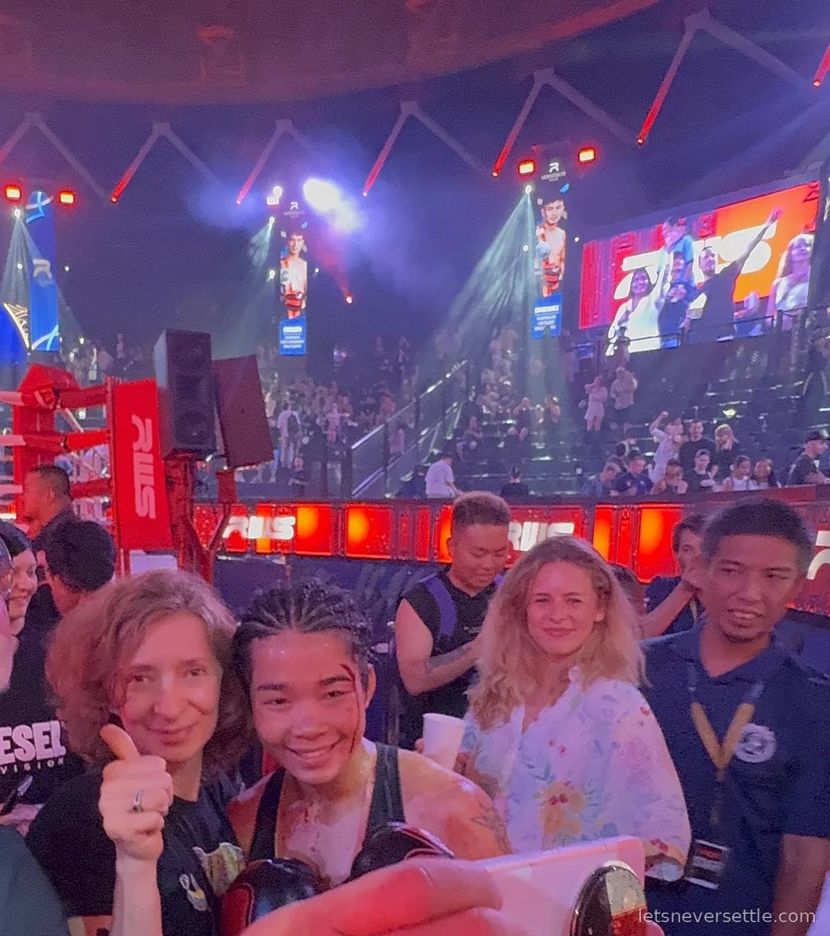 Inga giving a thumbs up beside a smiling female Muay Thai fighter with a cut above her eyebrow, ringside at Rajadamnern Stadium