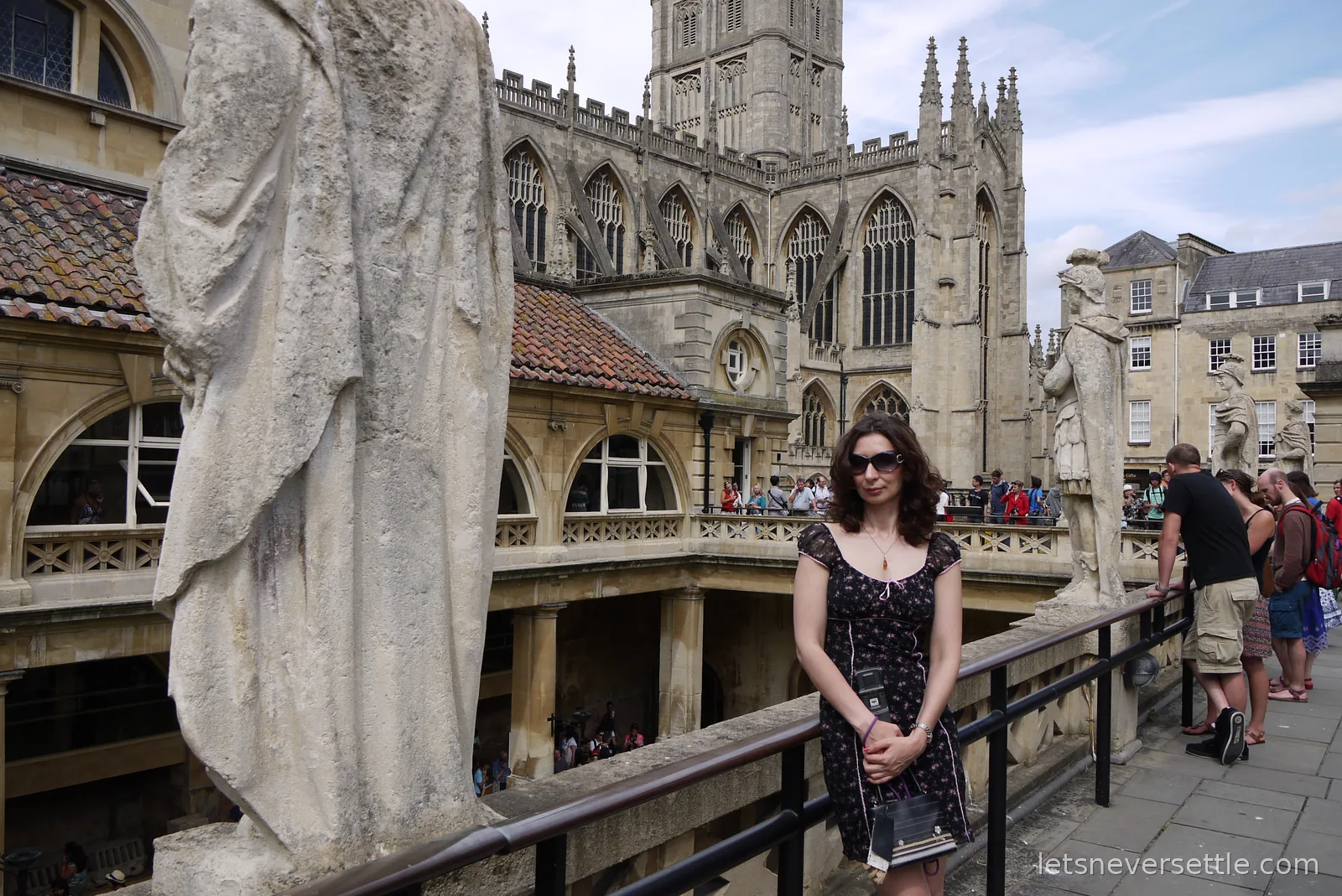 Inga standing on the statue-lined terrace of the Roman Baths with the tower of Bath Abbey rising behind