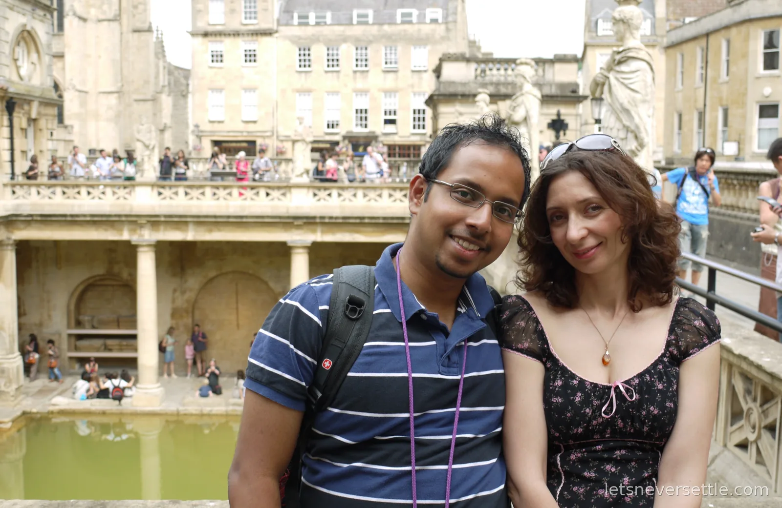 Inga and Dileep smiling at the railing above the green water of the Great Bath, visitors on the level below