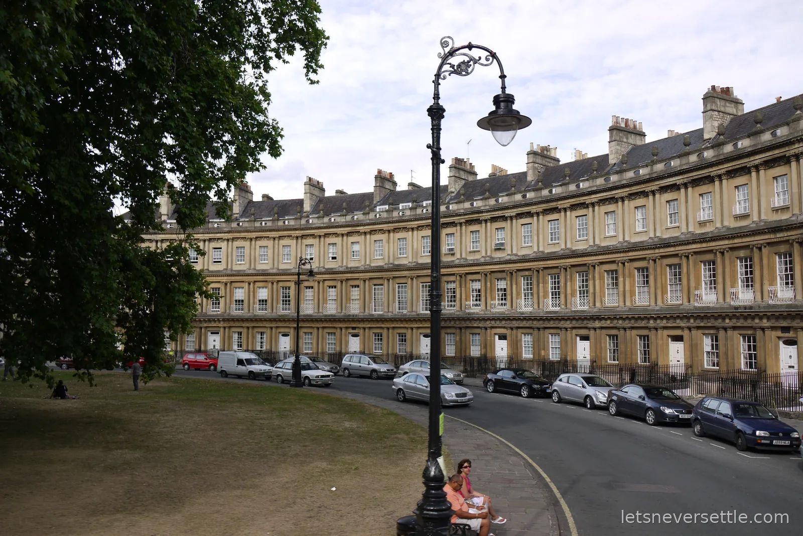 Sweeping curved Georgian terrace of honey-coloured stone in Bath with an ornate lamp post and a strip of green in front