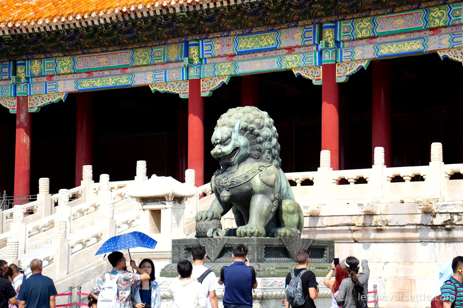 Bronze guardian lion with a paw on an orb in front of red columns and painted beams in the Forbidden City