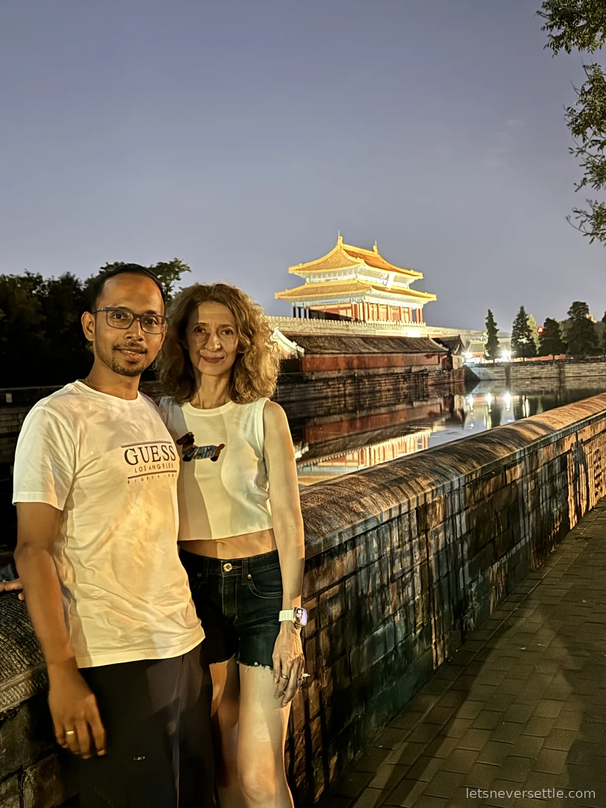 Inga and Dileep at dusk in front of the Forbidden City wall and gate tower, with the moat beside them