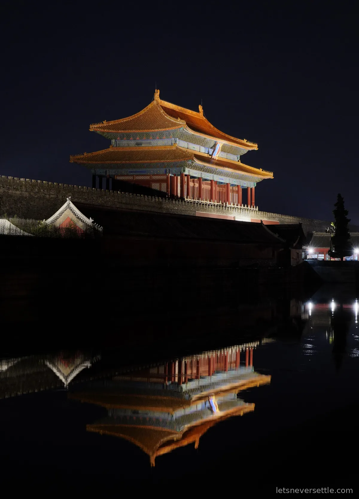 Illuminated gate tower of the Forbidden City at night, perfectly reflected in the still water of the moat