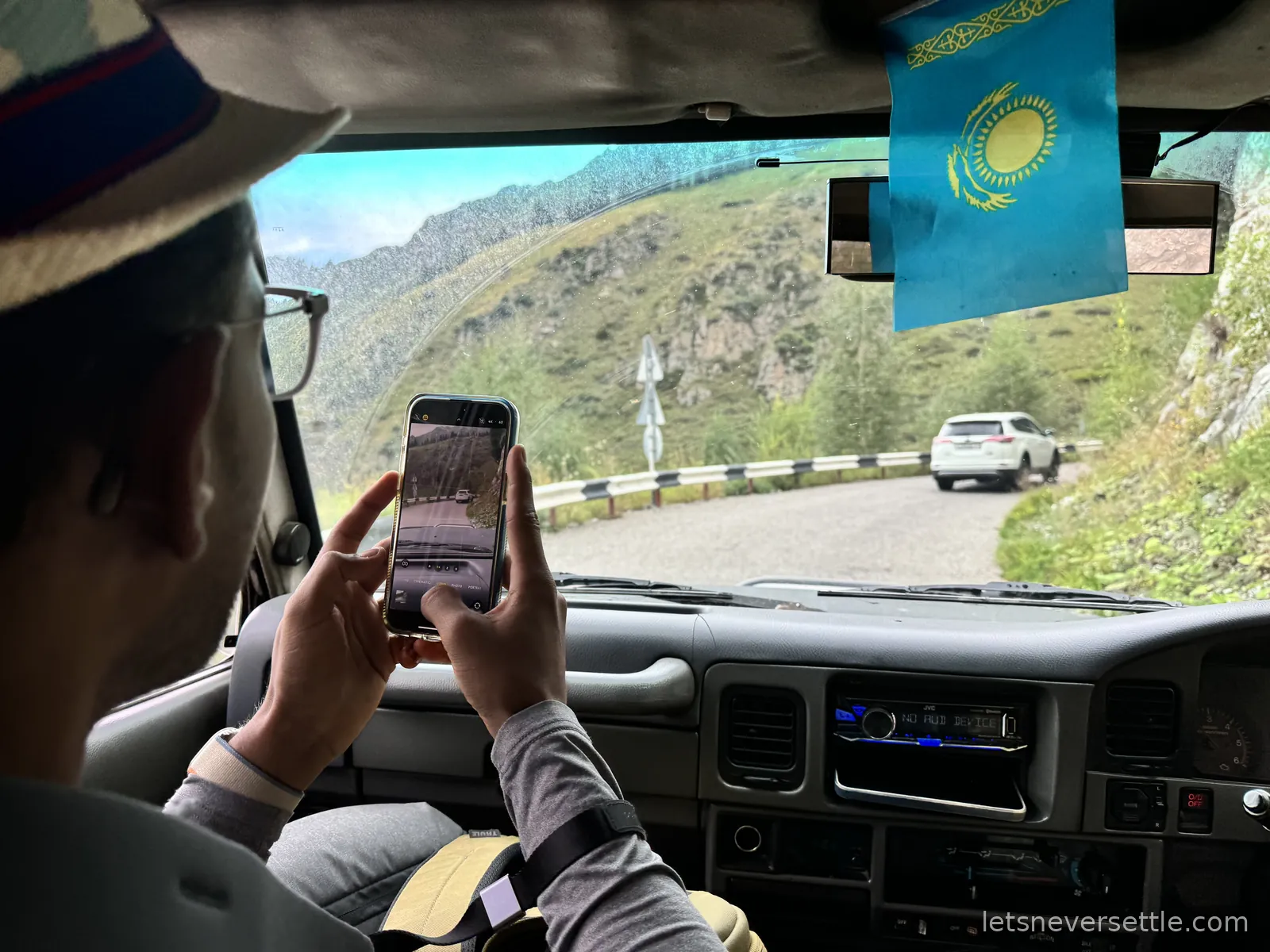 The view from inside the hired jeep, a Kazakh flag hanging from the mirror and another four wheel drive climbing the mountain road ahead