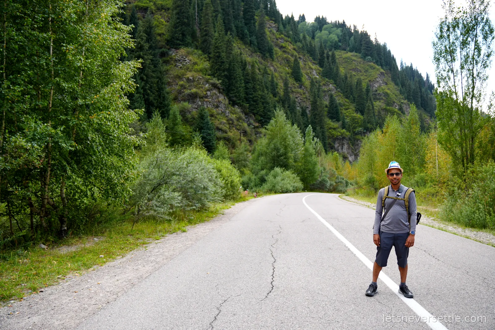 Dileep standing on the white line in the middle of the empty mountain road, wooded slopes rising on both sides