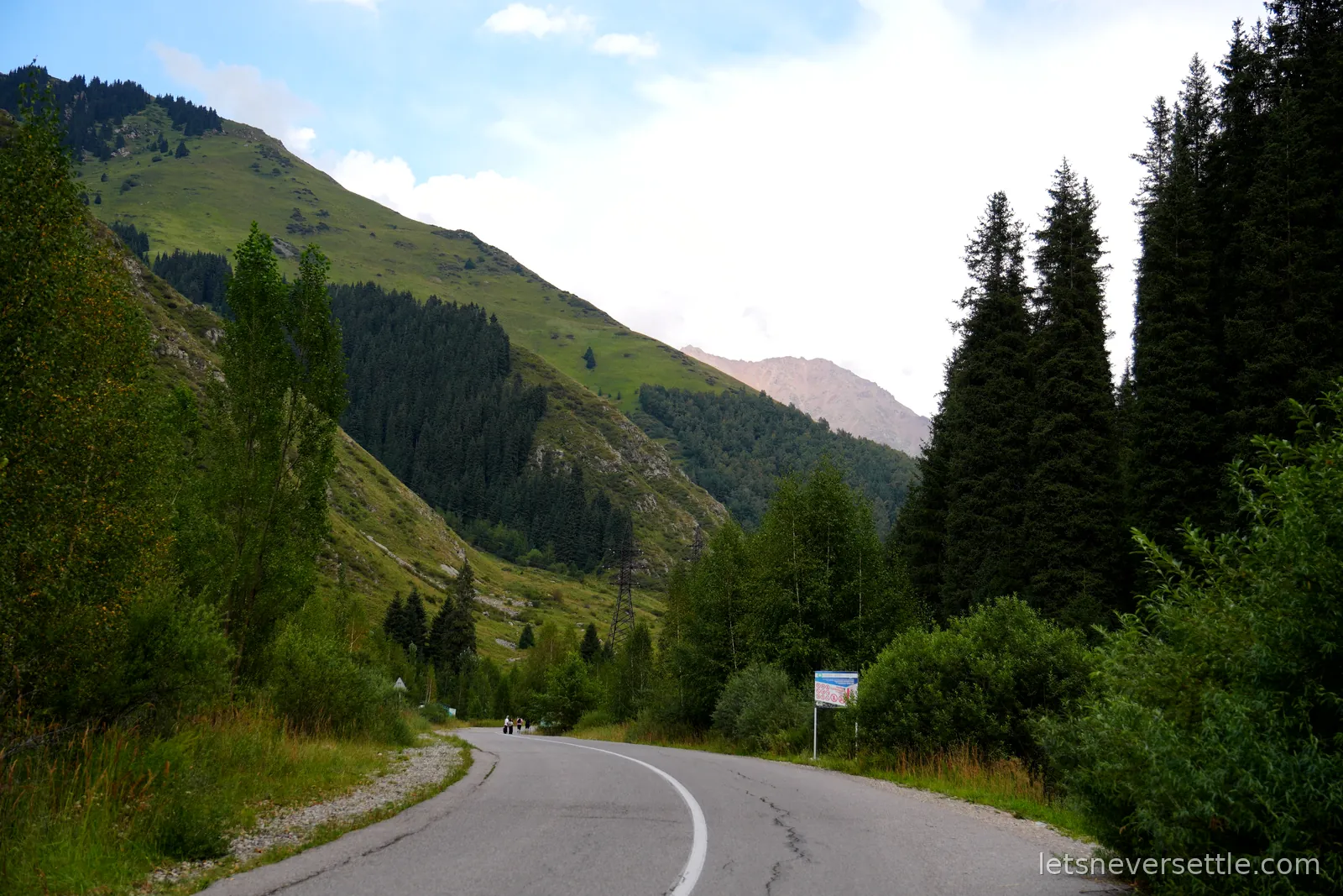 An empty tarmac road curving up a green valley between fir covered slopes on the way to Big Almaty Lake