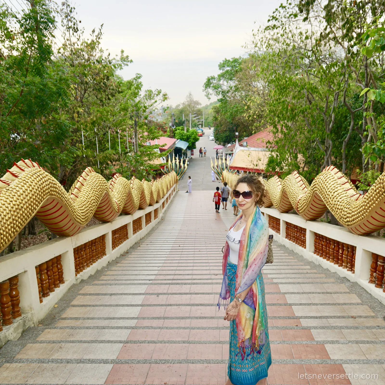 Inga standing at the top of the naga staircase at Big Buddha Hill looking back down the wide steps towards the street, parked cars and low rooftops below