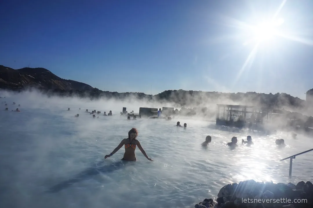 Inga wading through steaming milky-blue water at the Blue Lagoon, with bathers and dark hills behind