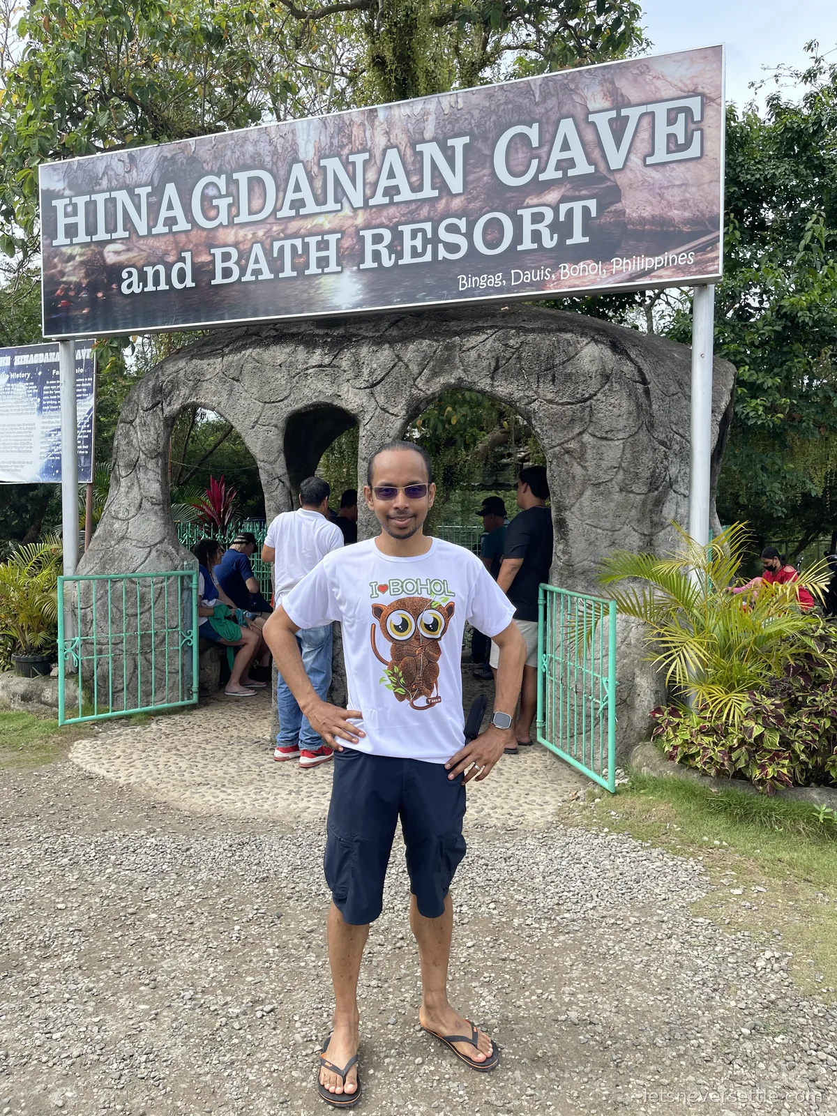 Dileep in a white I love Bohol tarsier t-shirt standing at the stone entrance arch of Hinagdanan Cave in Dauis