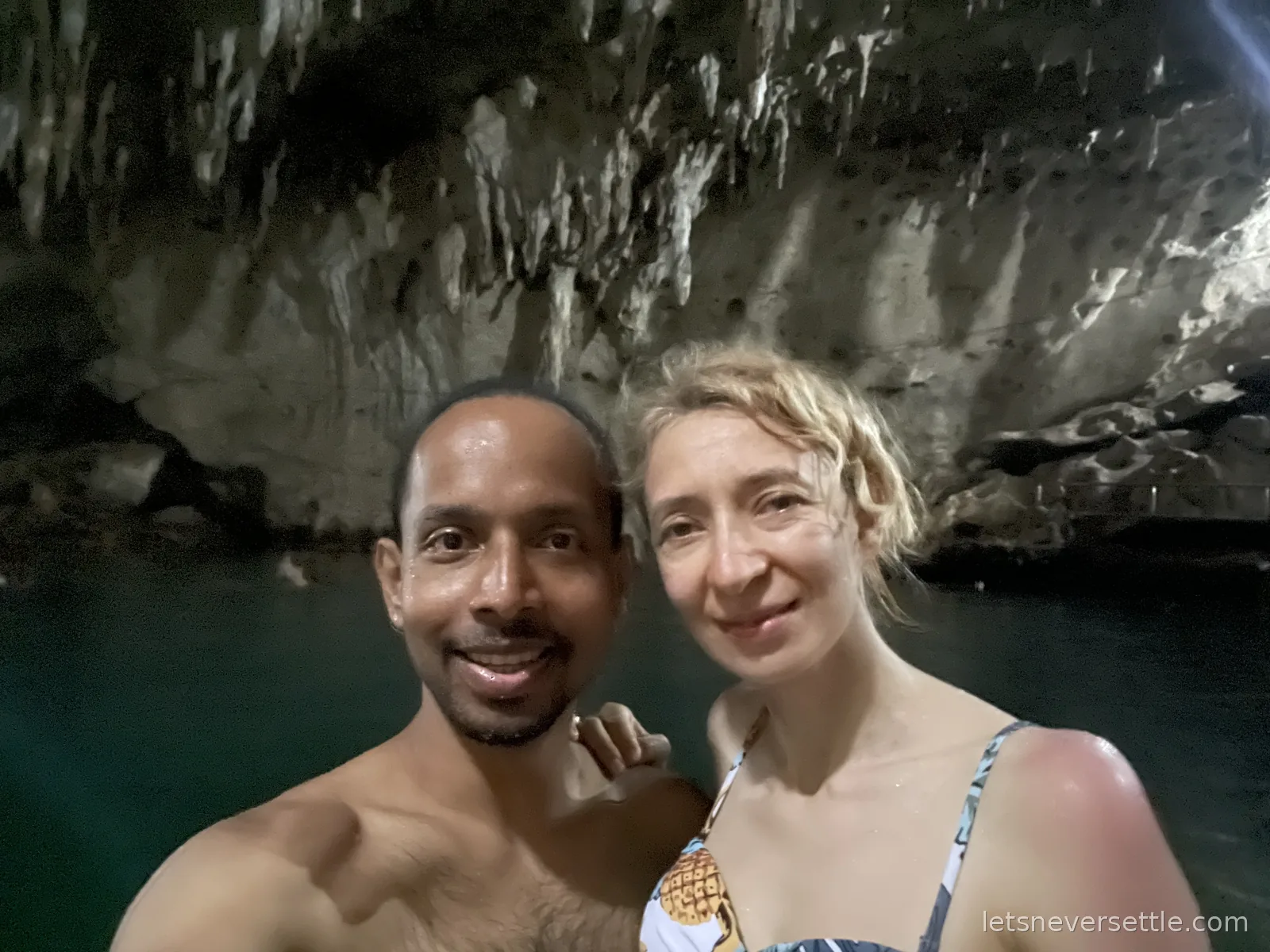 Selfie of Inga and Dileep swimming in the dark lagoon inside Hinagdanan Cave, stalactites hanging above the water