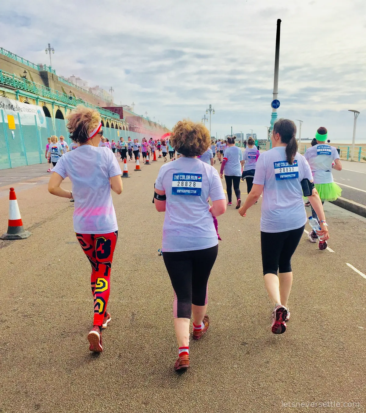 Runners in white Color Run T-shirts heading down Madeira Drive past Brighton's turquoise seafront arches