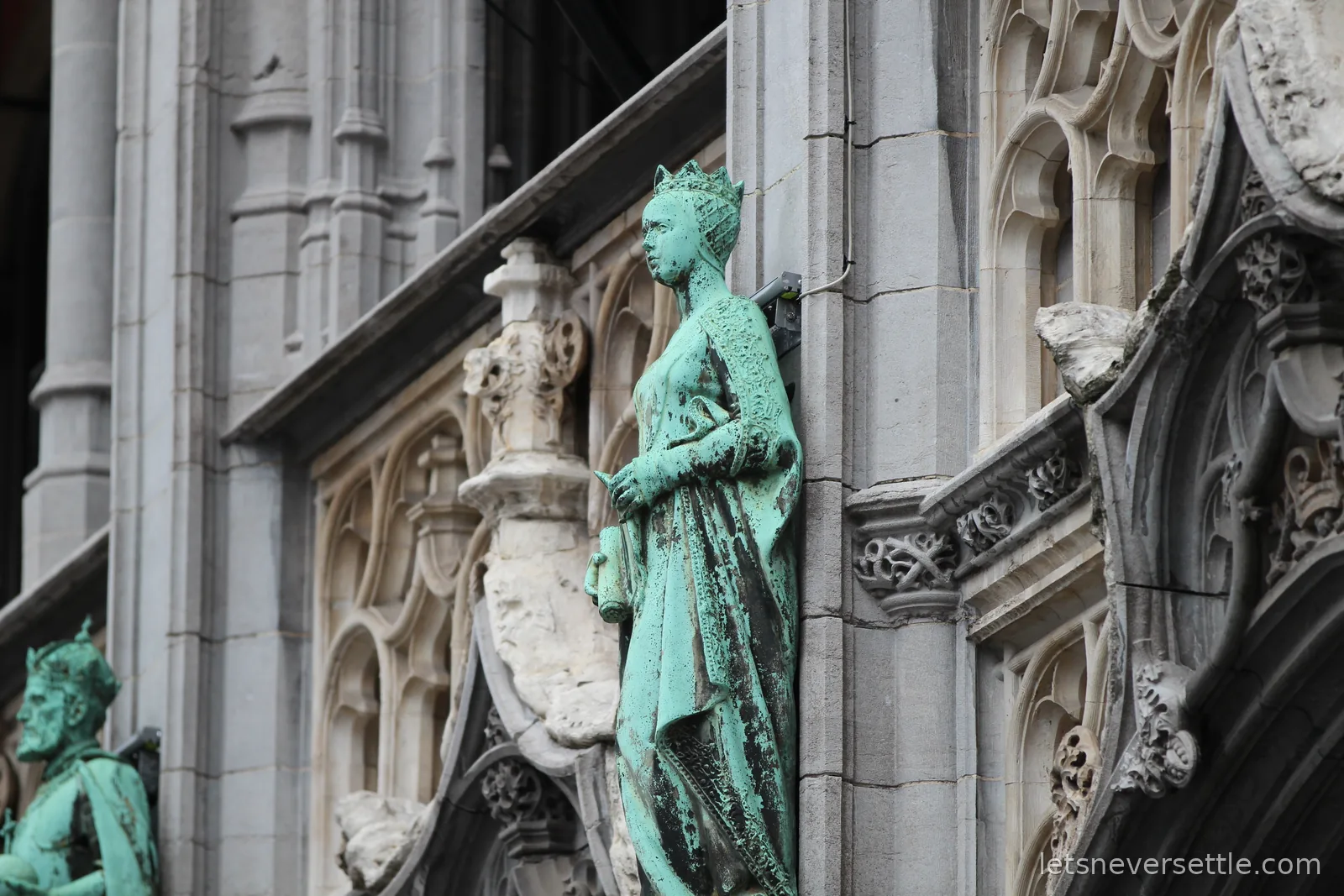 Crowned statues turned green with verdigris standing in niches on an ornate gothic stone facade in Brussels