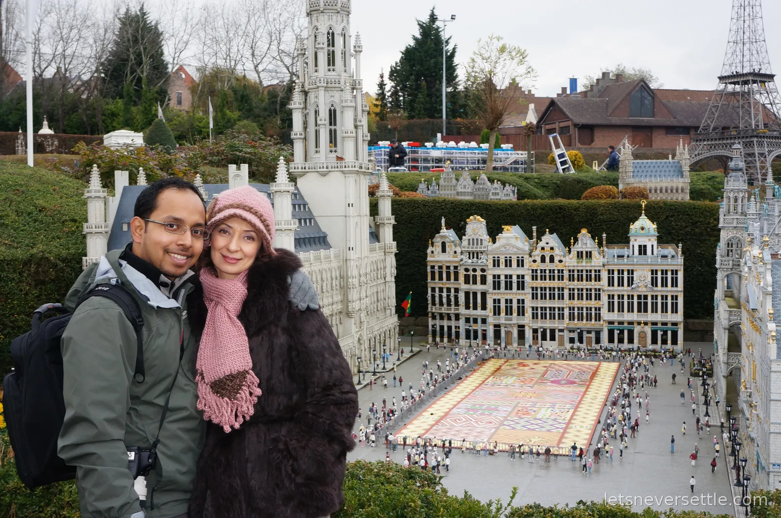 Dileep and Inga posing above the miniature Grand Place model with its flower carpet at Mini-Europe, a small Eiffel Tower in the background