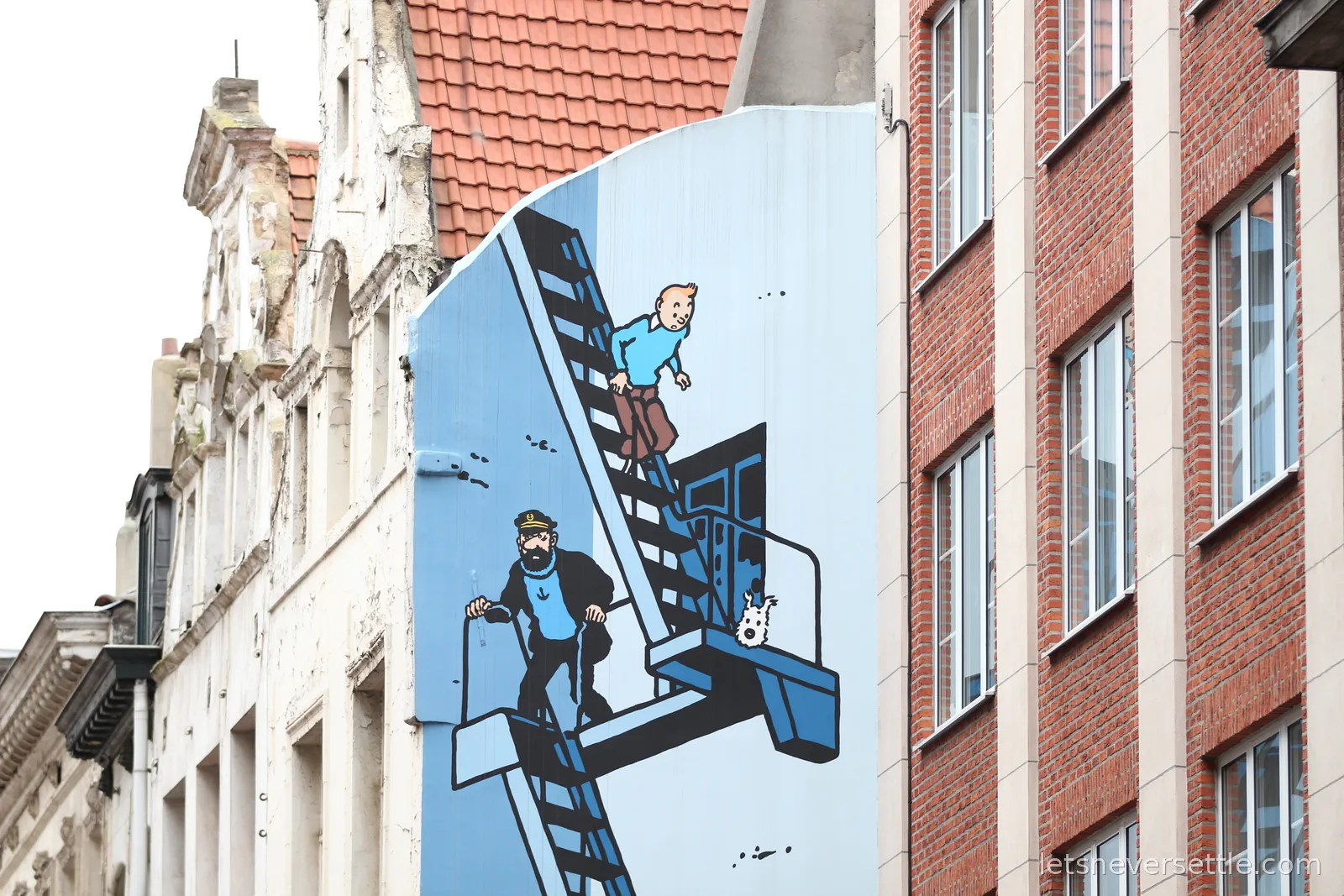 Large mural on a building gable showing Tintin, Captain Haddock and Snowy descending a fire escape