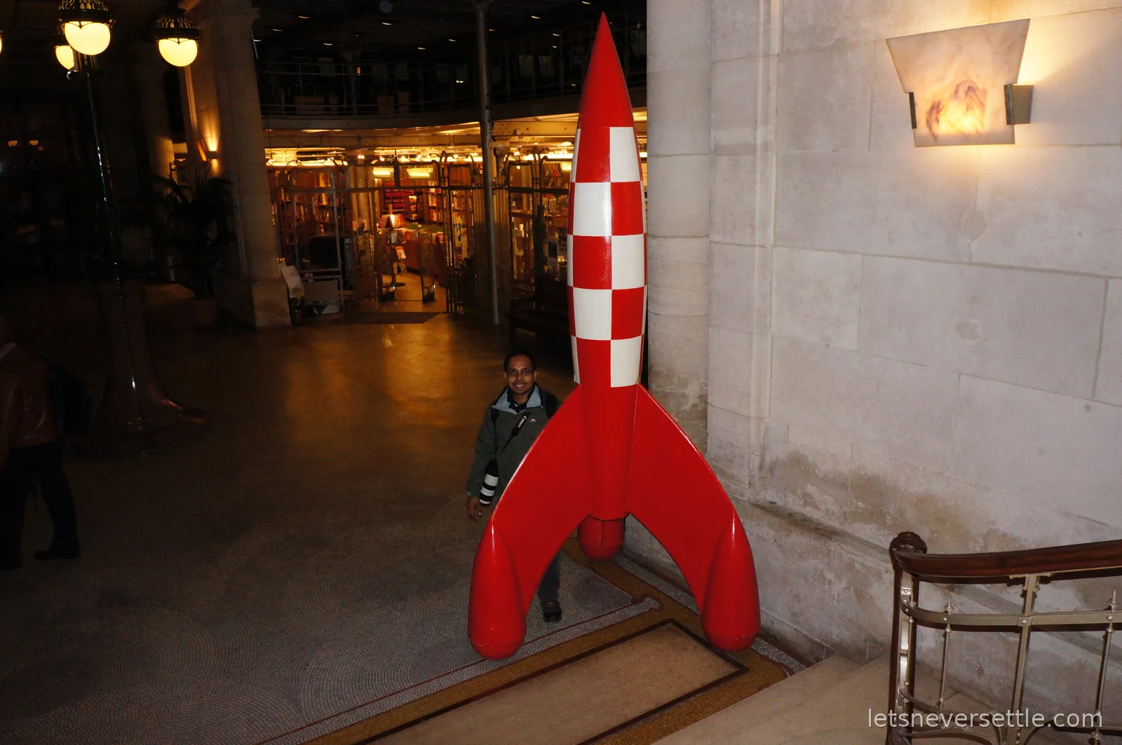 Dileep standing beside a tall red and white checkered Tintin moon rocket inside a grand arcade hall