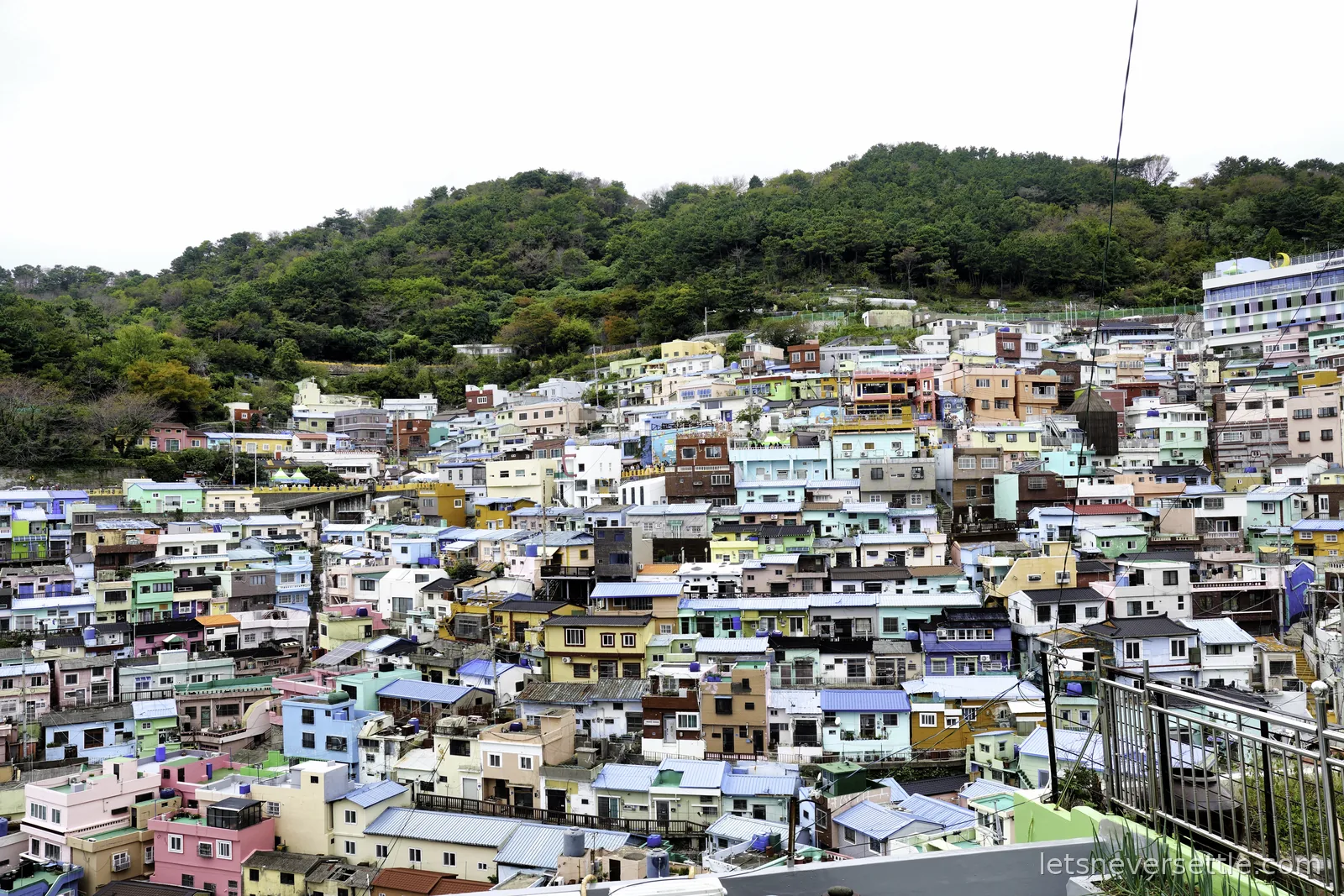 The pastel stacked houses of Gamcheon Culture Village covering a green hillside in Busan under a white sky