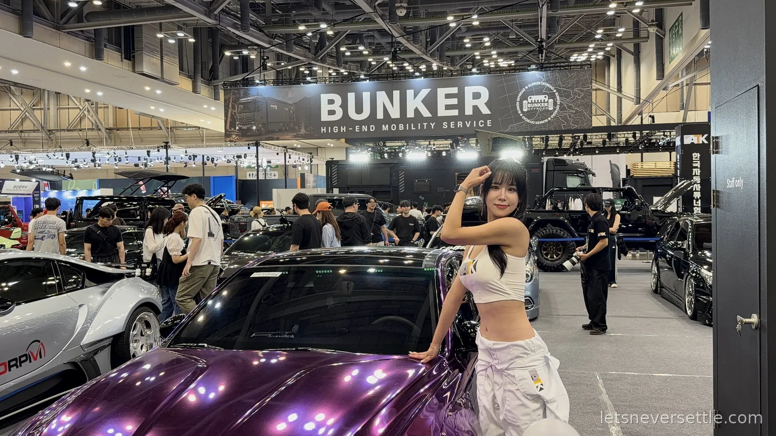 A purple chrome-wrapped car on the Bunker High-End Mobility Service stand at the Busan International Mobility Show, exhibition hall lights overhead