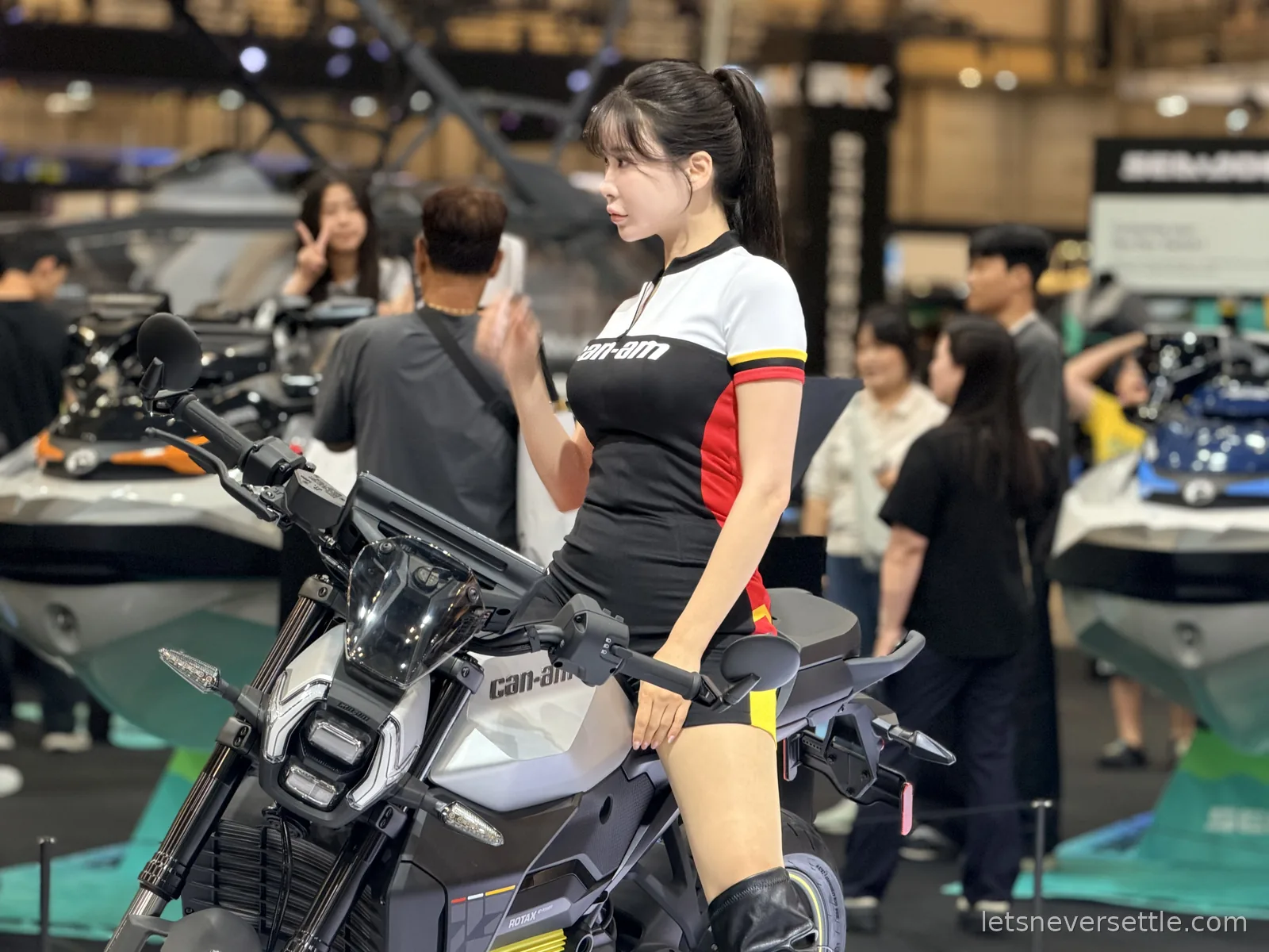Close view of a Can-Am electric motorcycle on display at the Busan International Mobility Show, visitors moving around the hall behind