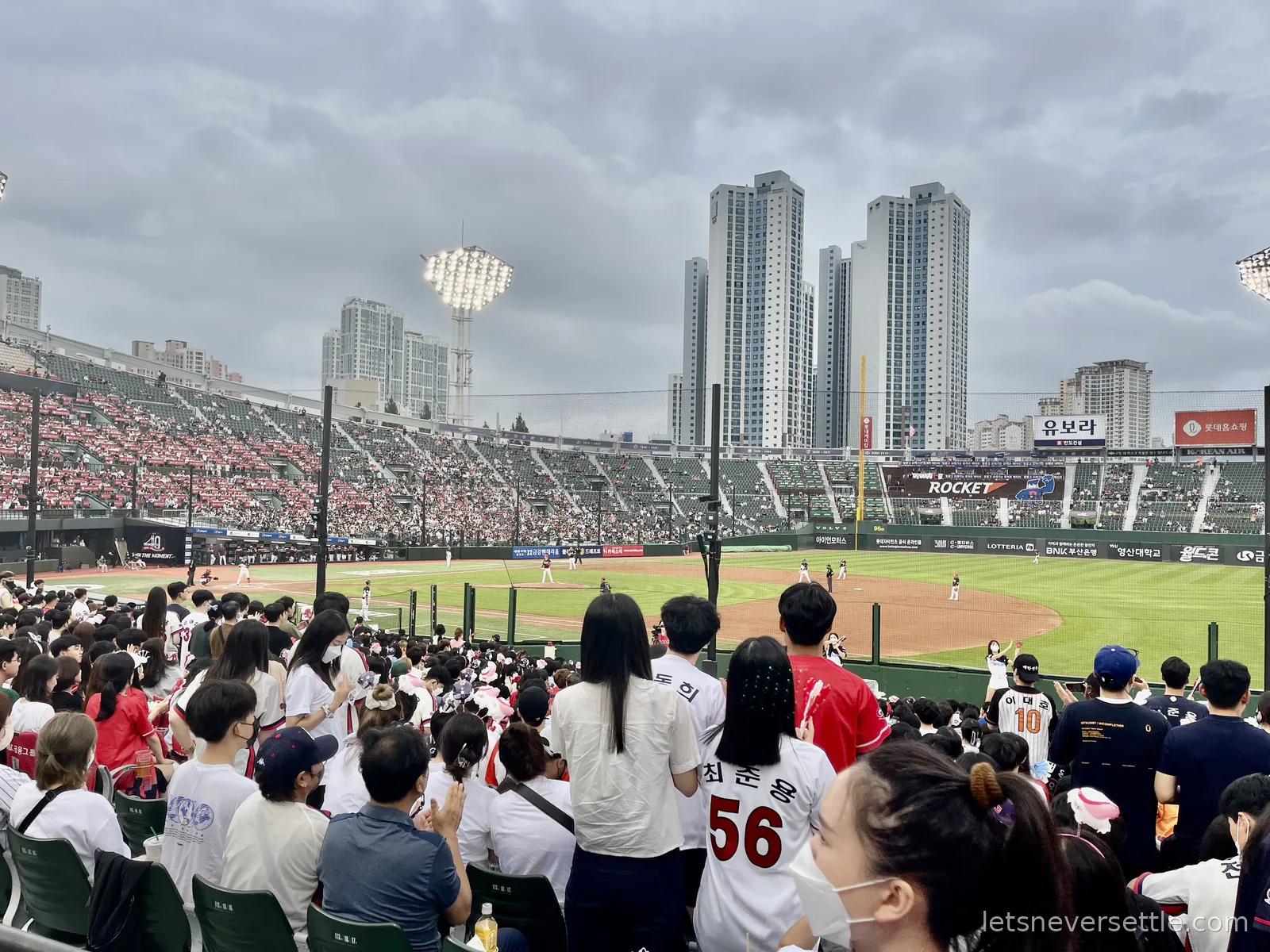 Crowd in baseball jerseys watching a game at Sajik Stadium in Busan, floodlights on under a grey sky