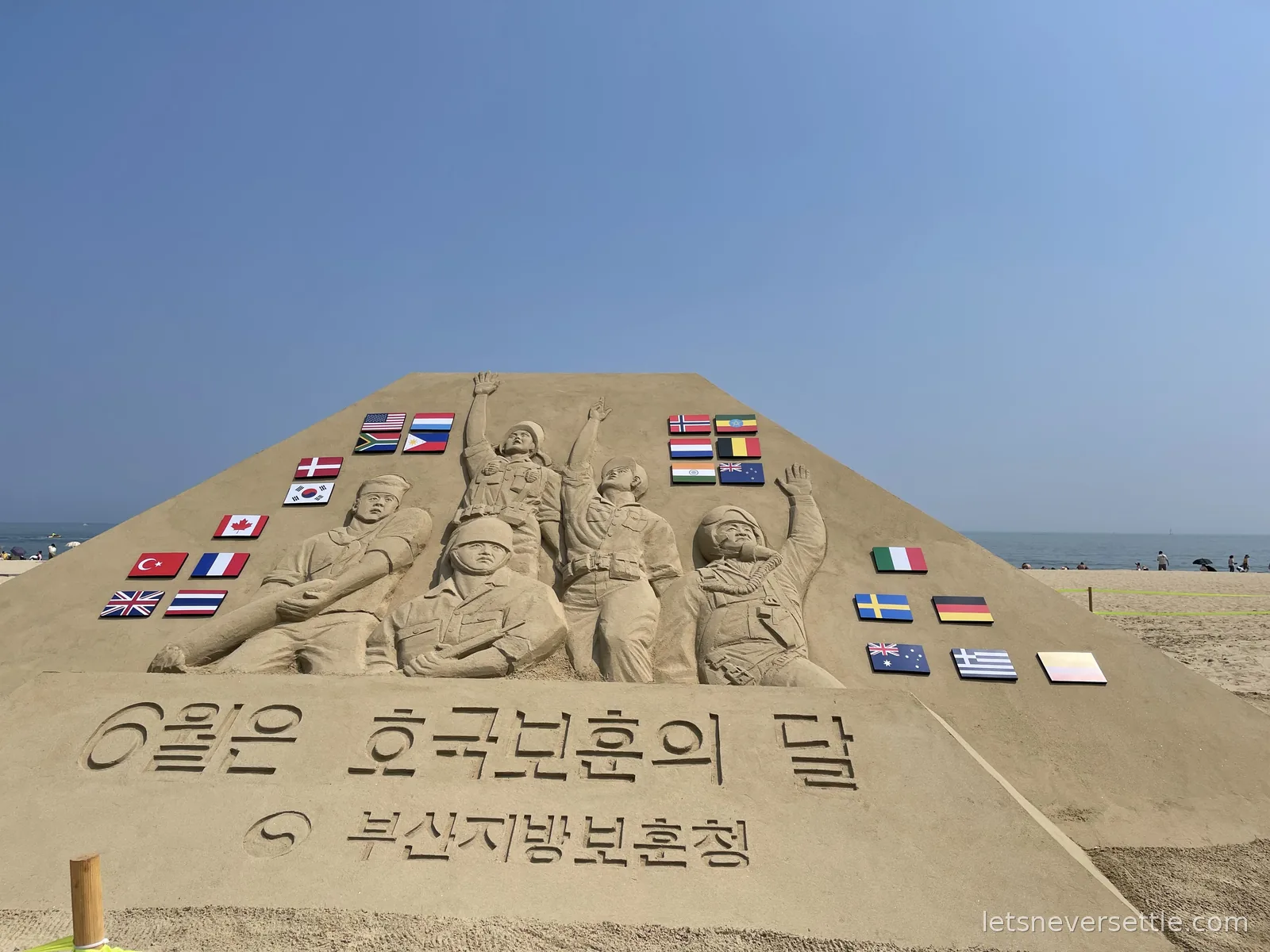 Large sand sculpture of soldiers on Haeundae beach, decorated with the flags of many nations