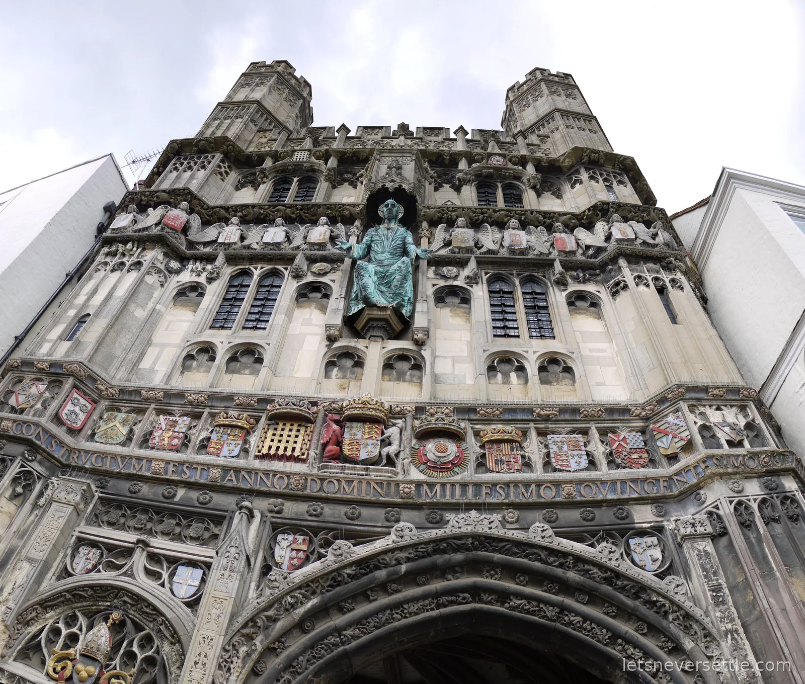 Christ Church Gate in Canterbury, an ornate Tudor gateway covered in painted heraldic shields with a green statue of Christ above the arch