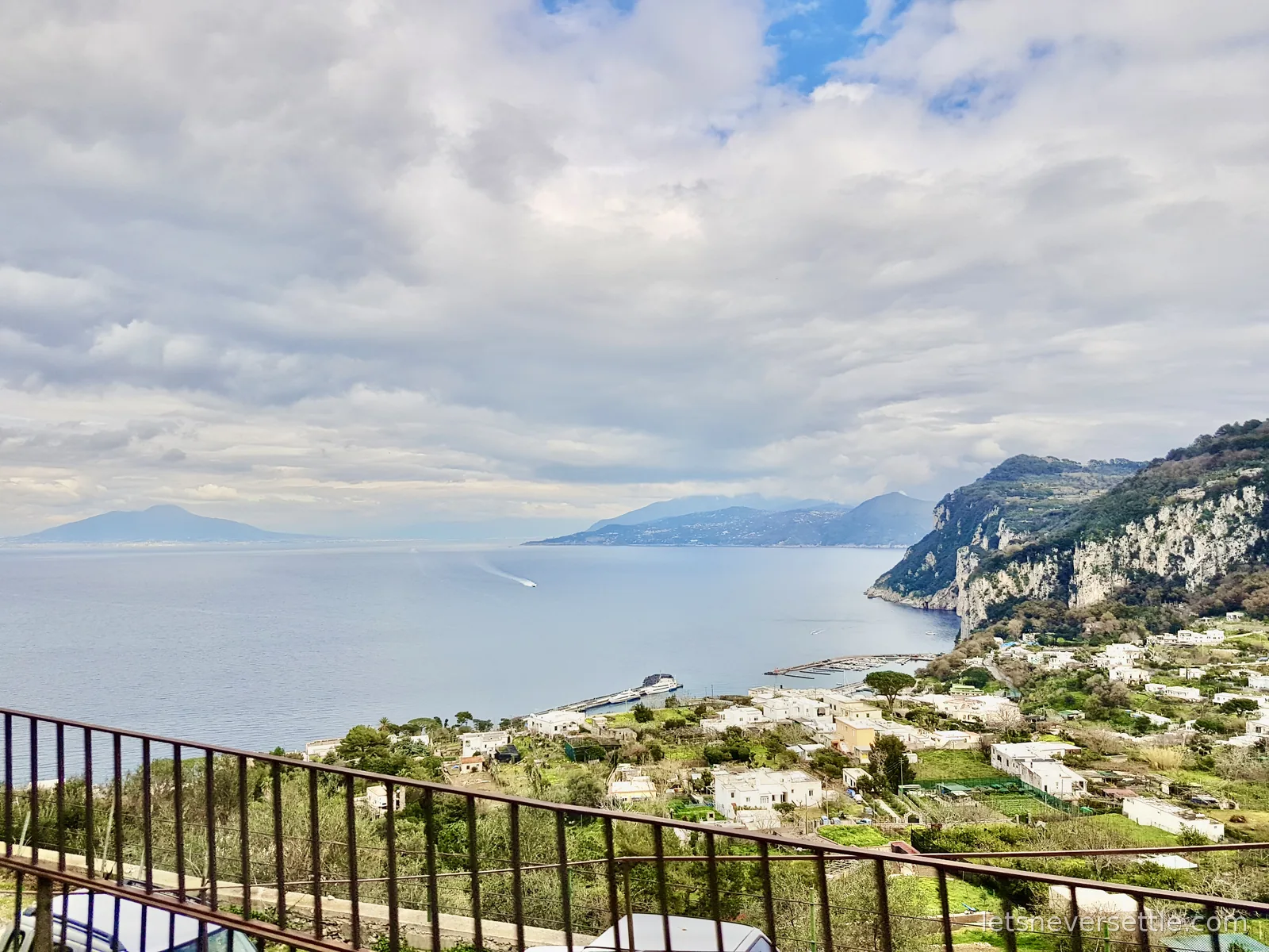 A high view over the sea from Capri, with the marina and terraced houses below, the mainland coast and a headland in the distance