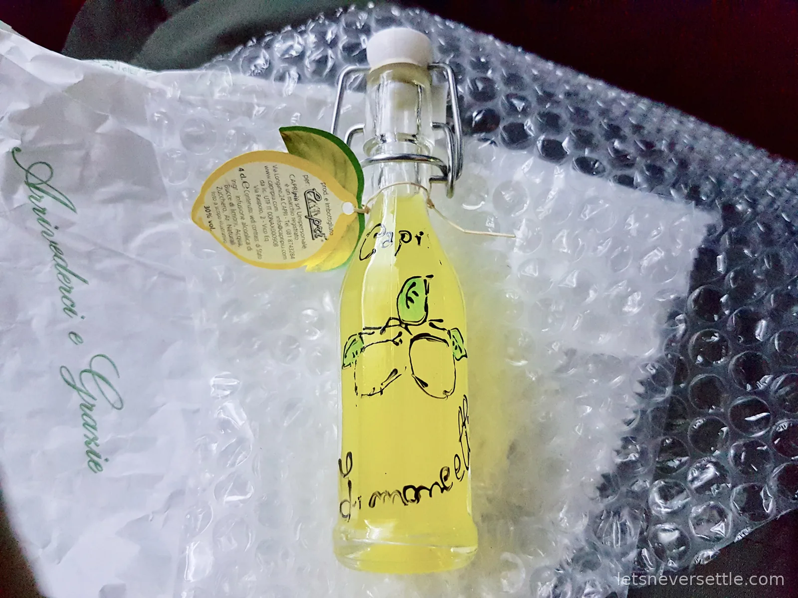 A swing top bottle of bright yellow limoncello with a lemon shaped label, wrapped in bubble wrap on a paper bag printed Arrivederci e Grazie