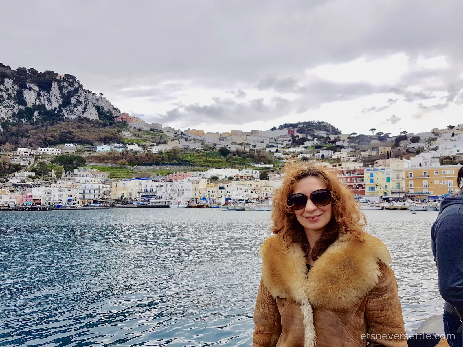Inga on a boat in the harbour at Capri, with the pastel houses of Marina Grande and the green hillside rising steeply behind her