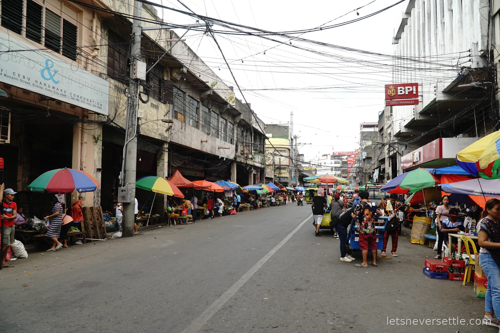 A long street in Cebu City lined with market stalls under bright umbrellas, shoppers filling the road and cables strung overhead