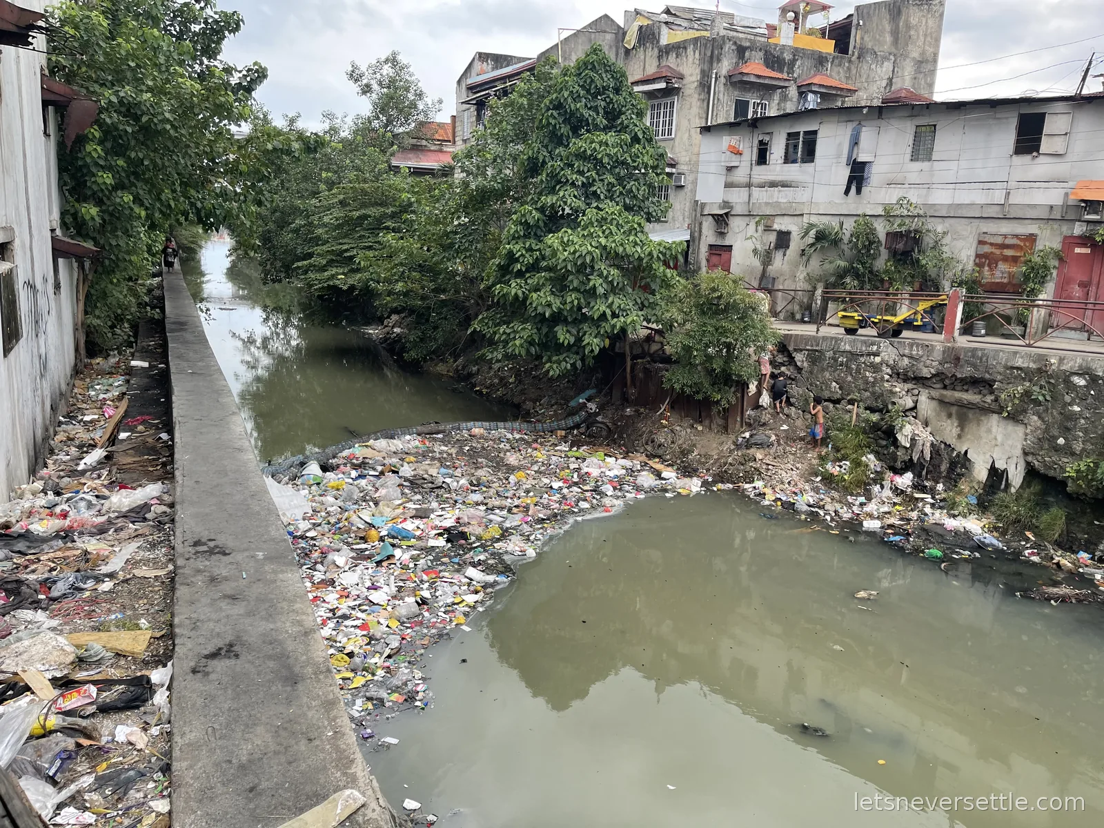 A city canal between old houses with a raft of plastic waste floating on the green water