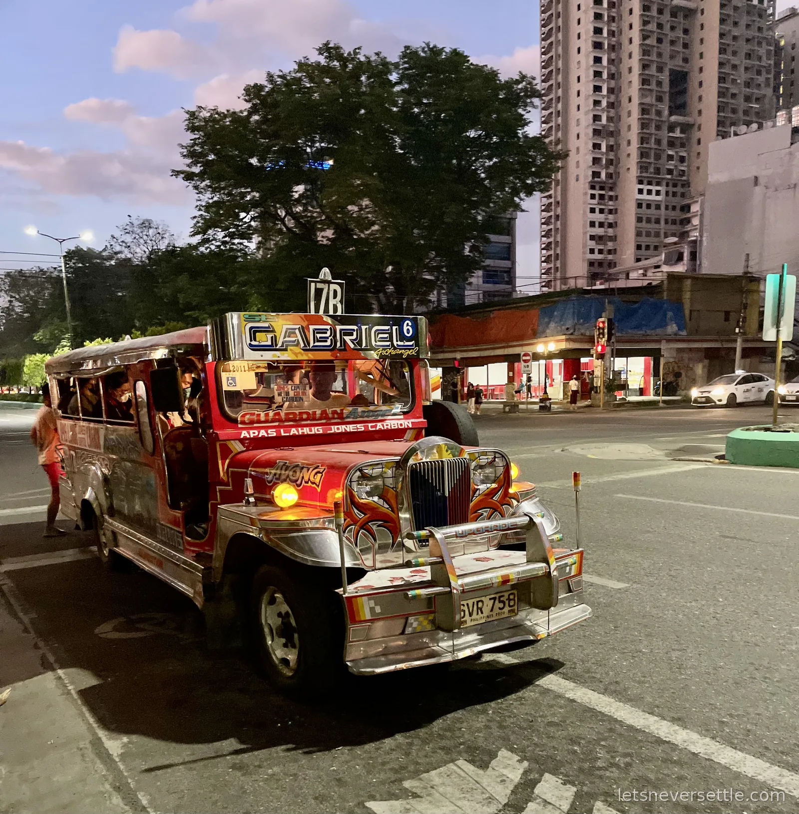 A red jeepney with a chrome nose and the route board Apas Lahug Jones Carbon collecting passengers at dusk in Cebu City