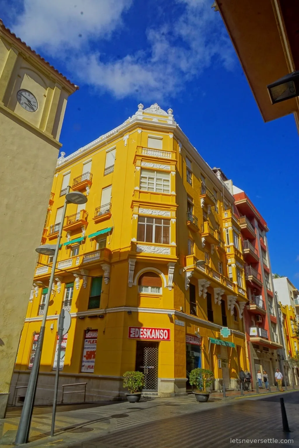 A bright egg-yellow modernist corner building with white stucco detail under a deep blue sky