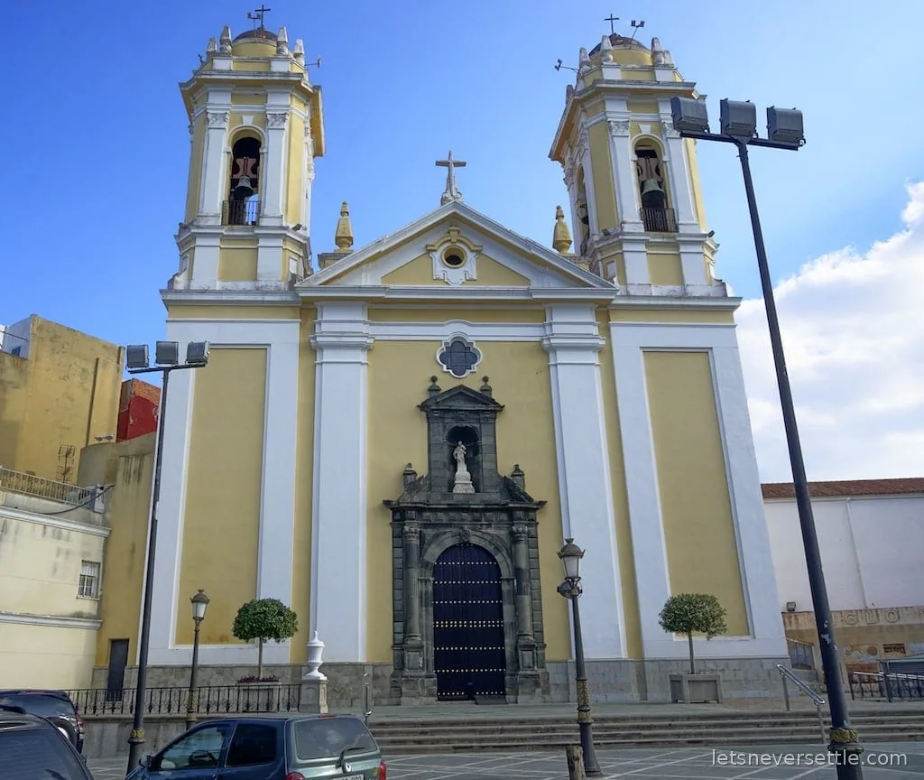 The yellow and white facade of Ceuta Cathedral with twin bell towers and a dark stone portal