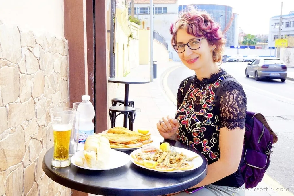 Inga at a street cafe table with plates of fried fish, bread and a glass of beer